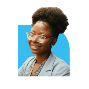 Headshot of Nikki. She has brown hair which is tied up. She is wearing glasses, a light blue jacket and a black and white striped top.